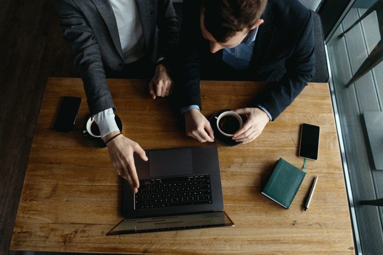 Dois homens de negócios apotando para notebook e discutindo sobre competências empreendedoras