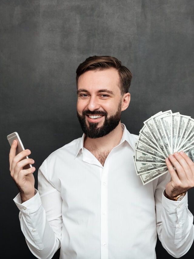 Homem de camisa social branca segurando notas de dólar em uma mão e na outra o celular