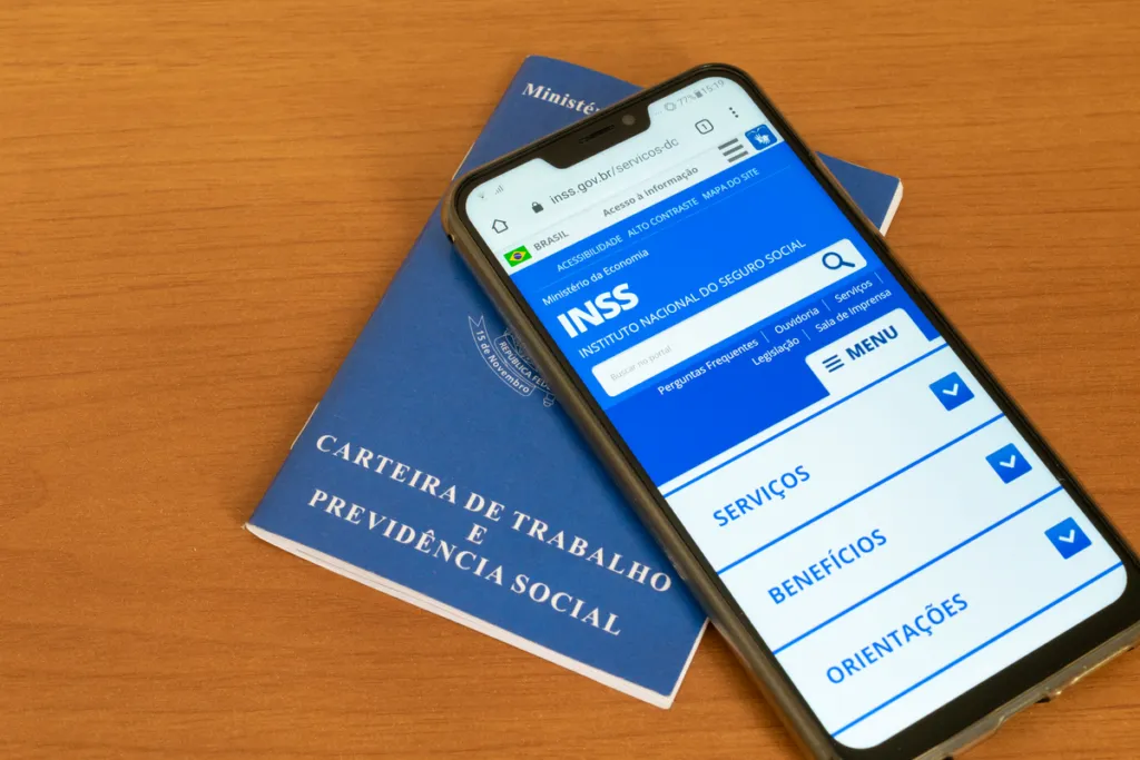 Um celular acessando a página do INSS sob uma carteira de trabalho em uma mesa