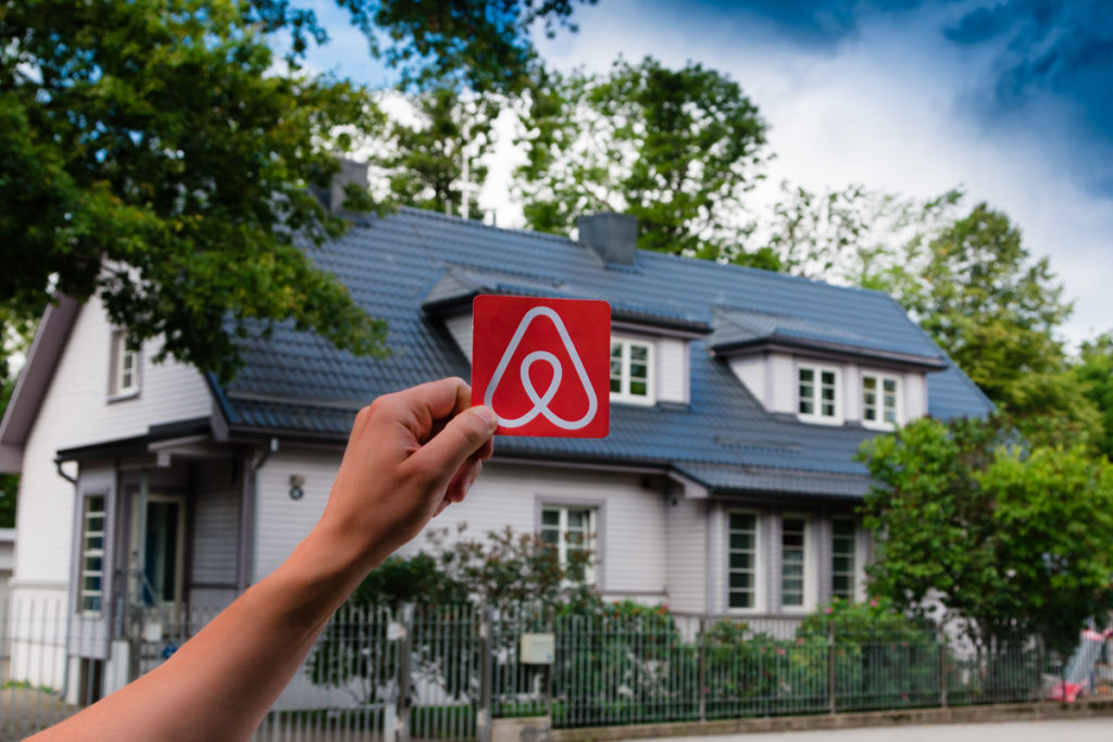 homem segurando o selo do airbnb em frente de uma casa 