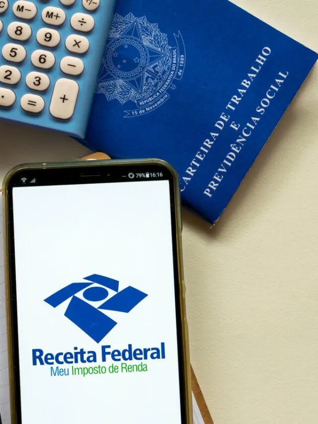 Uma mesa vista de cima com um celular acessando o site da Receita Federal, um carteira de trabalho e uma calculadora