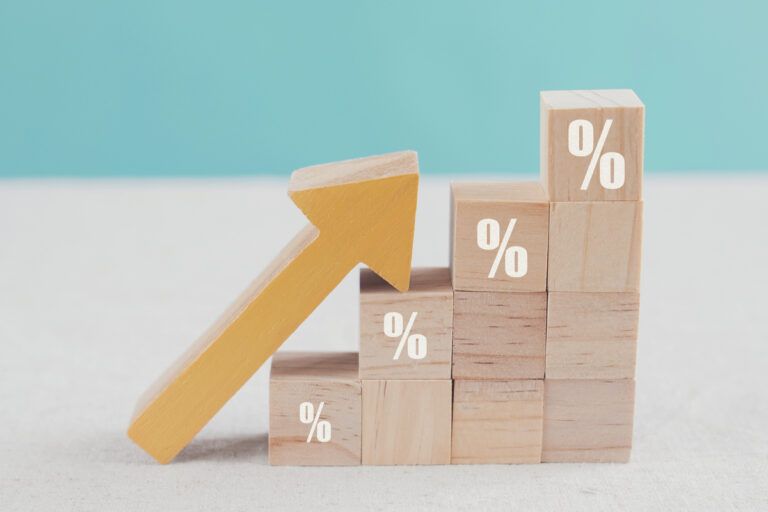 pecinhas de madeiras com símbolo de percentagem e uma seta indicando o crescimento da inflação em cima da mesa