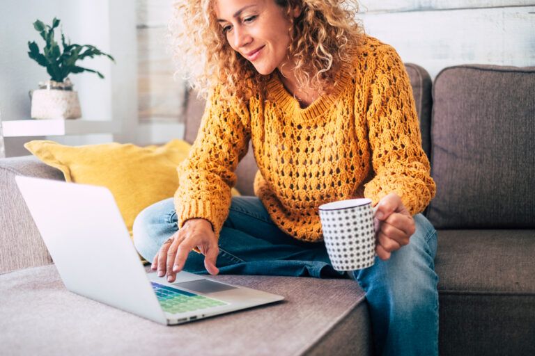 mulher acessando no computador a plataforma Fansly enquanto toma café