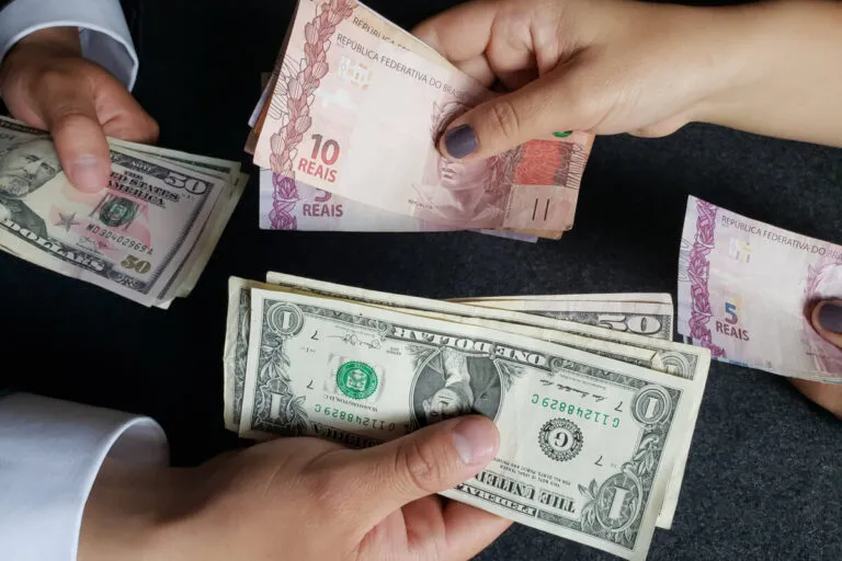 duas pessoas trocando notas de reais por notas de dólar