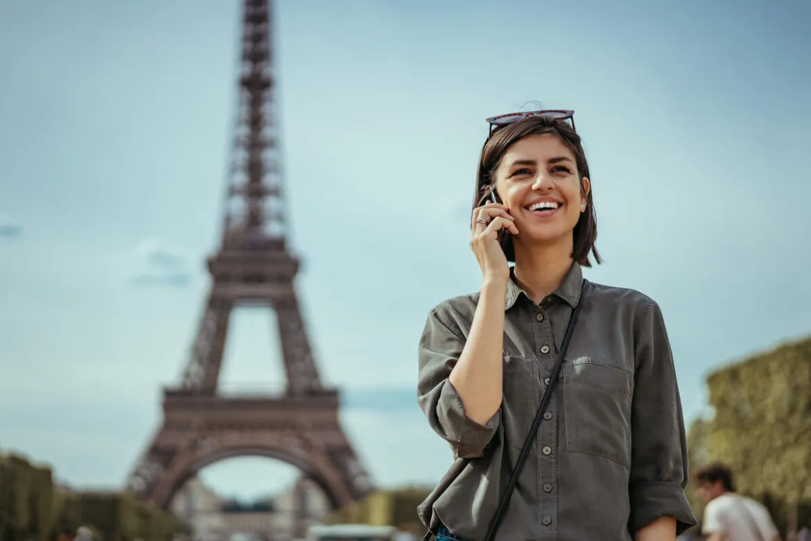 Uma moça falando ao telefone com a Torre Eiffel às suas costas