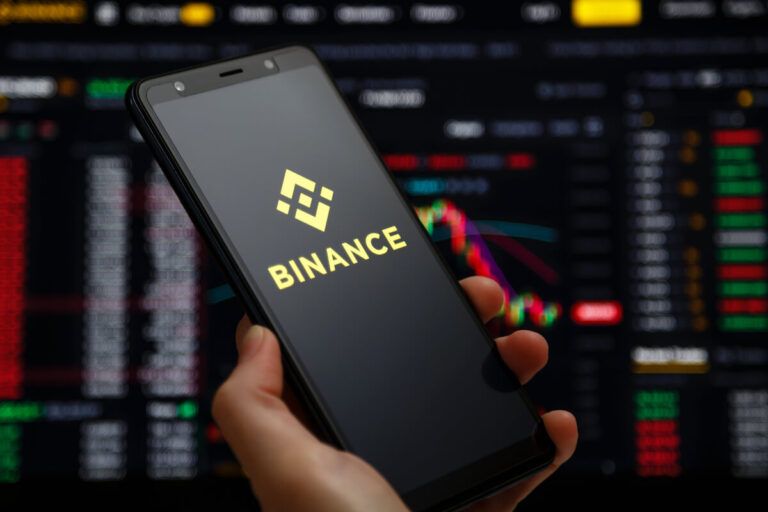 Um smartphone com o logo da Binance e um dashboard ao fundo