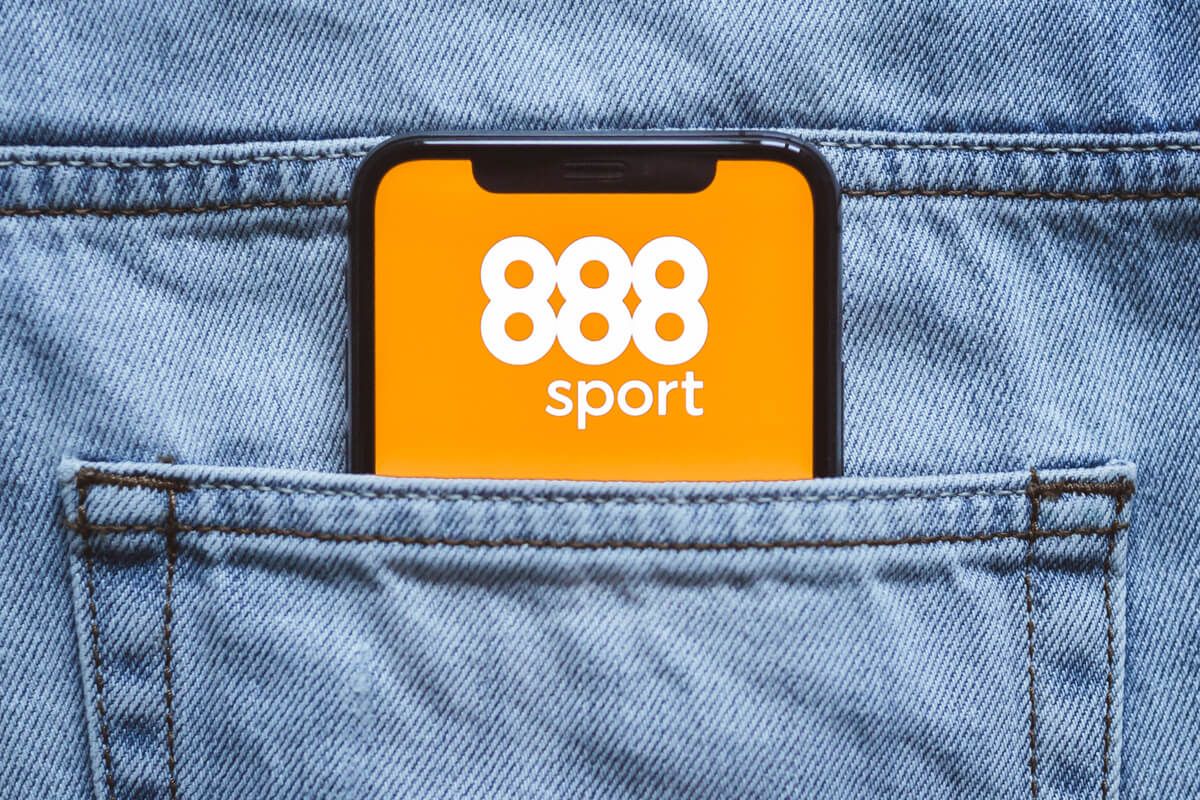 Imagem de um smartphone com o logo do 888 Sports na tela, dentro do bolso de uma calça