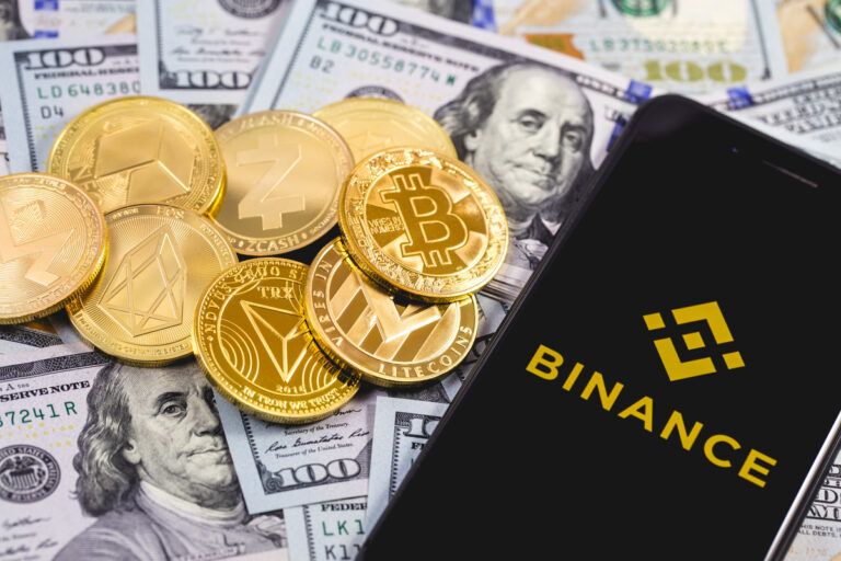 Moedas de bitcoin e notas de dólar com um smartphone ao lado com o logo da Binance