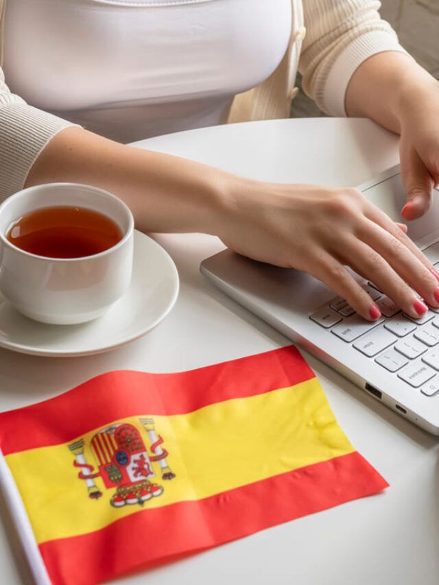 Mulher mexendo no computador com uma bandeira da Espanha do lado