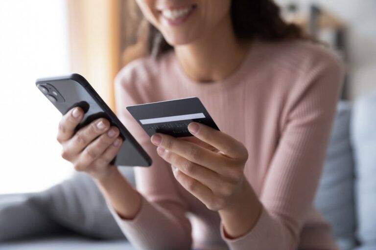 Mulher sorrindo olhando para o telefone e um cartão de crédito