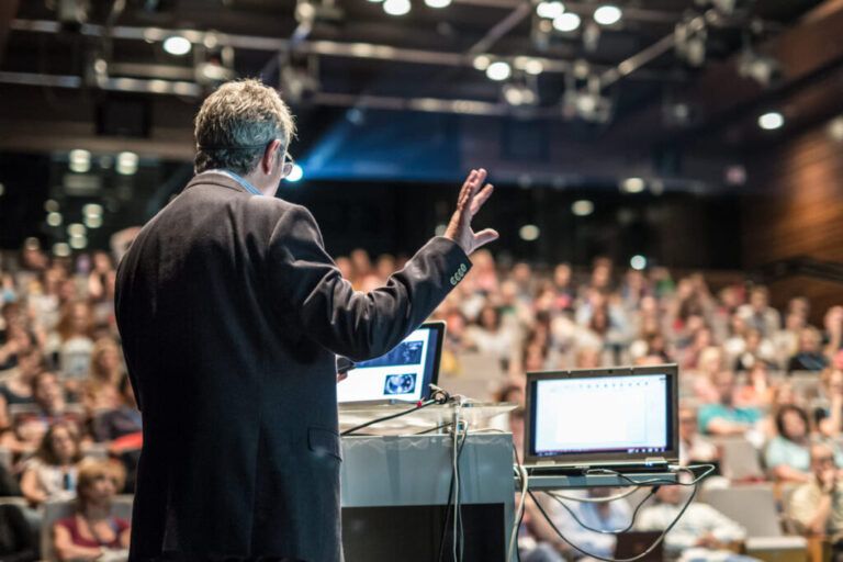 A imagem mostra uma palestra em um palco no estilo do Meeting Comex 2023