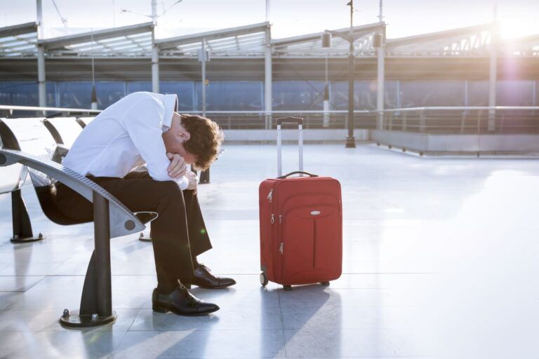 Um homem branco sentado no aeroporto, frustrado por causa de um voo cancelado.