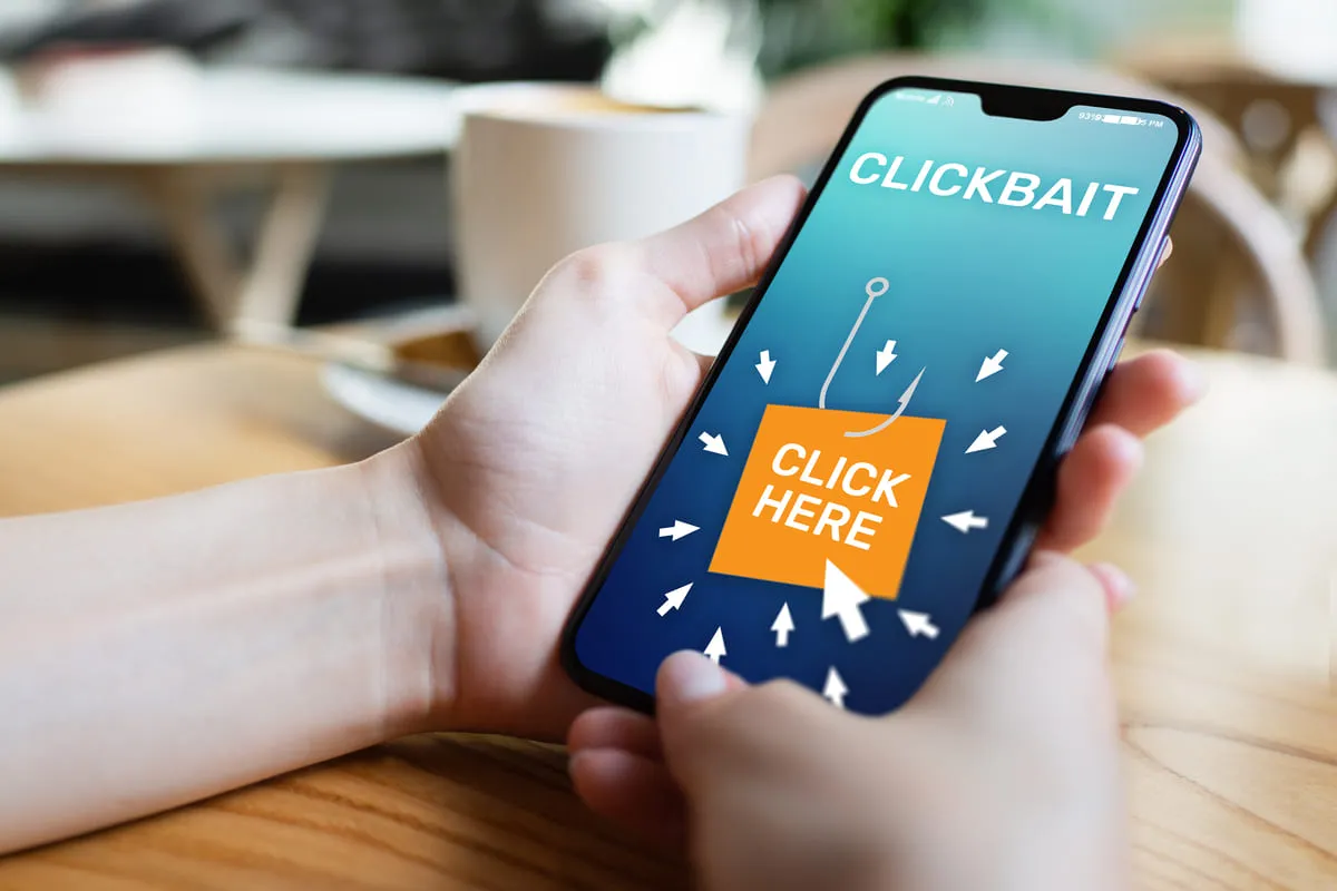 Duas mãos brancas segurando um smarthphone com a mensagem "clickbait"