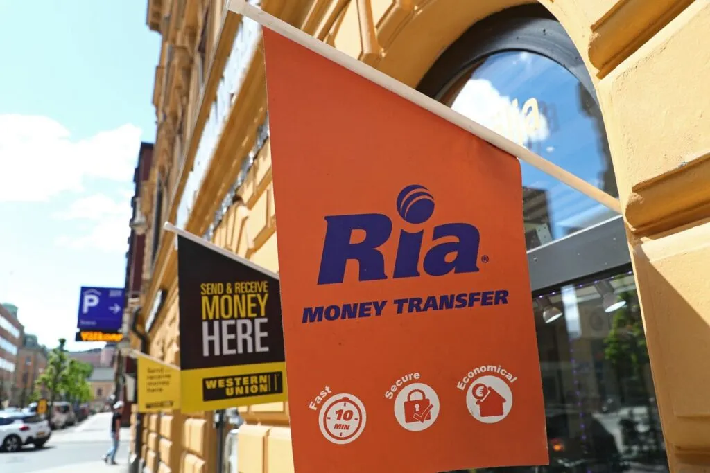 Banner com logo da Ria Money Transfer em uma agência da empresa. 