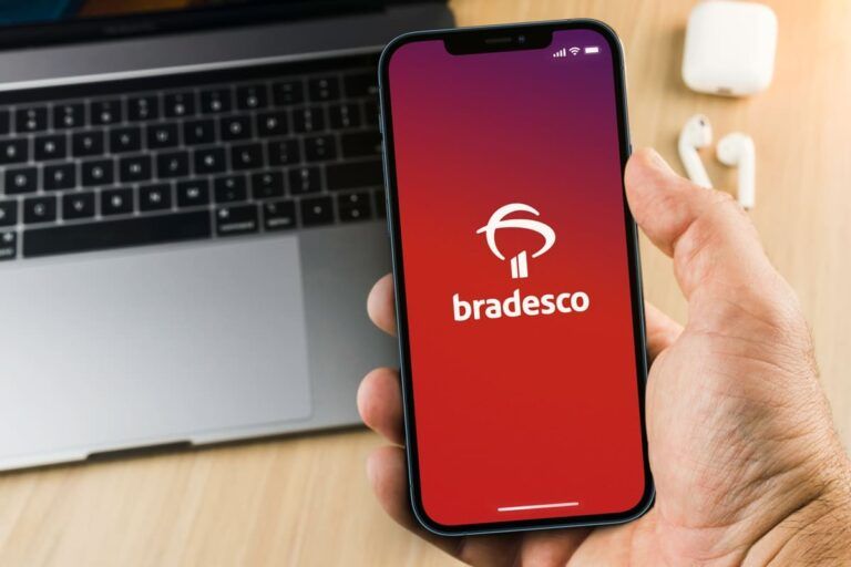 Mão masculina segurando um smartphone com o aplicativo do Banco Bradesco na tela, para ilustrar o bradesco fora do ar.