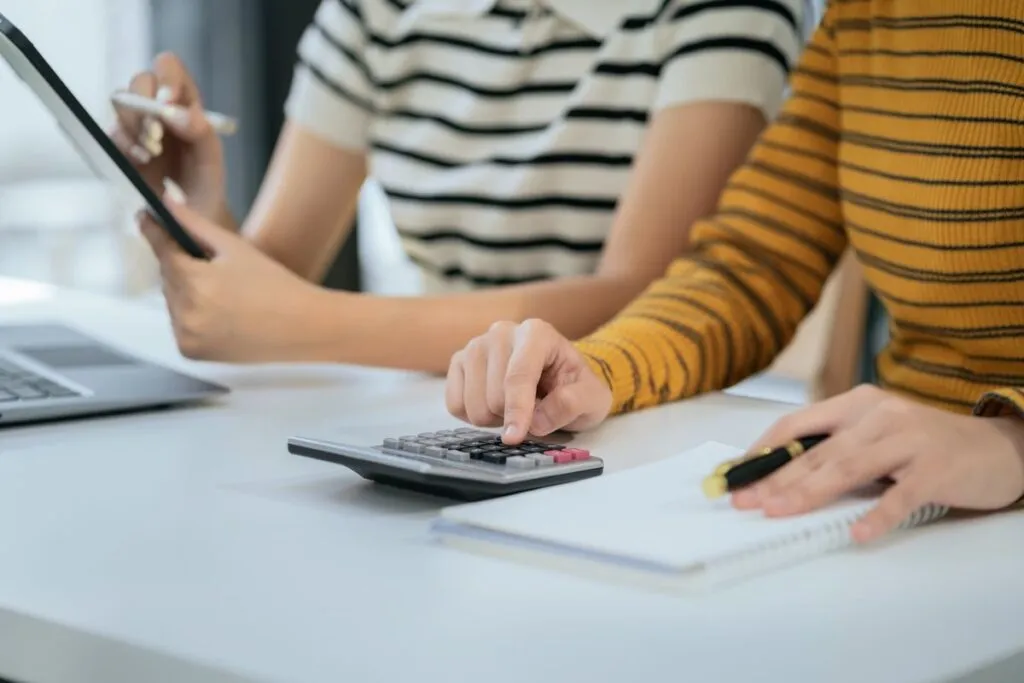 Mulheres calculando as taxas na calculadora e tablet. 