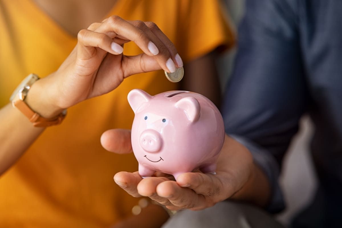 Pessoas colocando moeda em cofre após aprender a como economizar dinheiro.