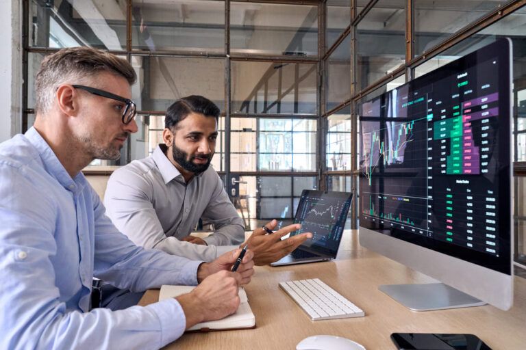 Dois homens observando gráficos de investimentos para ilustrar um texto sobre o que é CRA