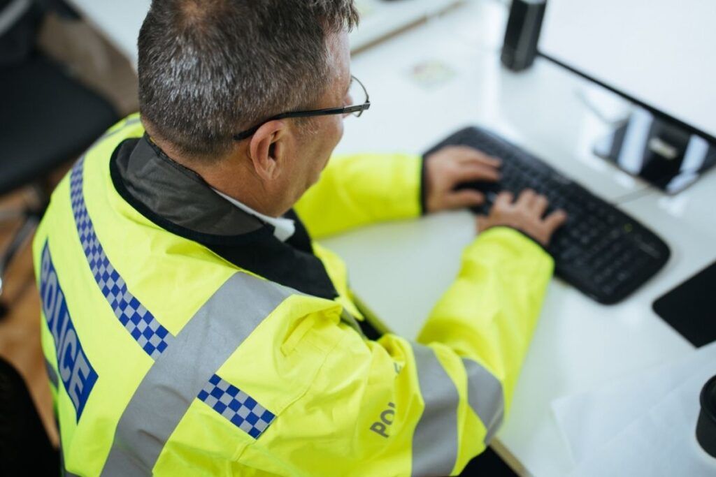 Policial de costas digitando boletim de ocorrência.