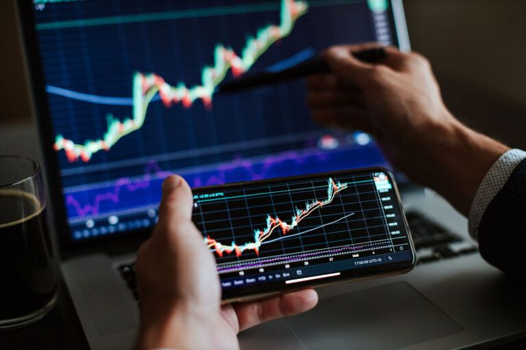 Tela de computador e celular com trading de investimentos