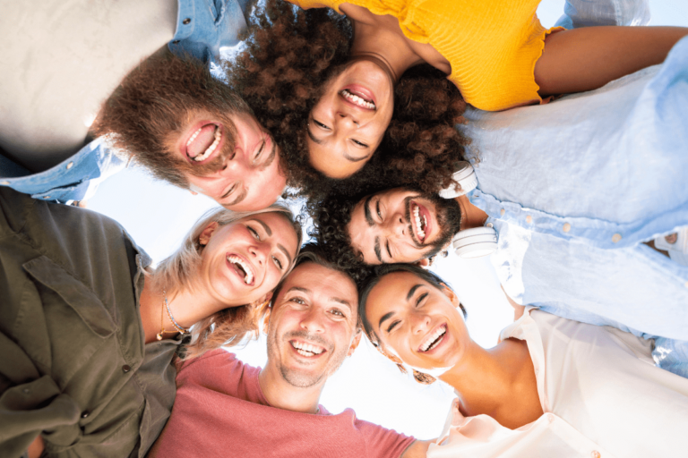 Grupo de seis amigos sorridentes formando um círculo e olhando para baixo para a câmera.