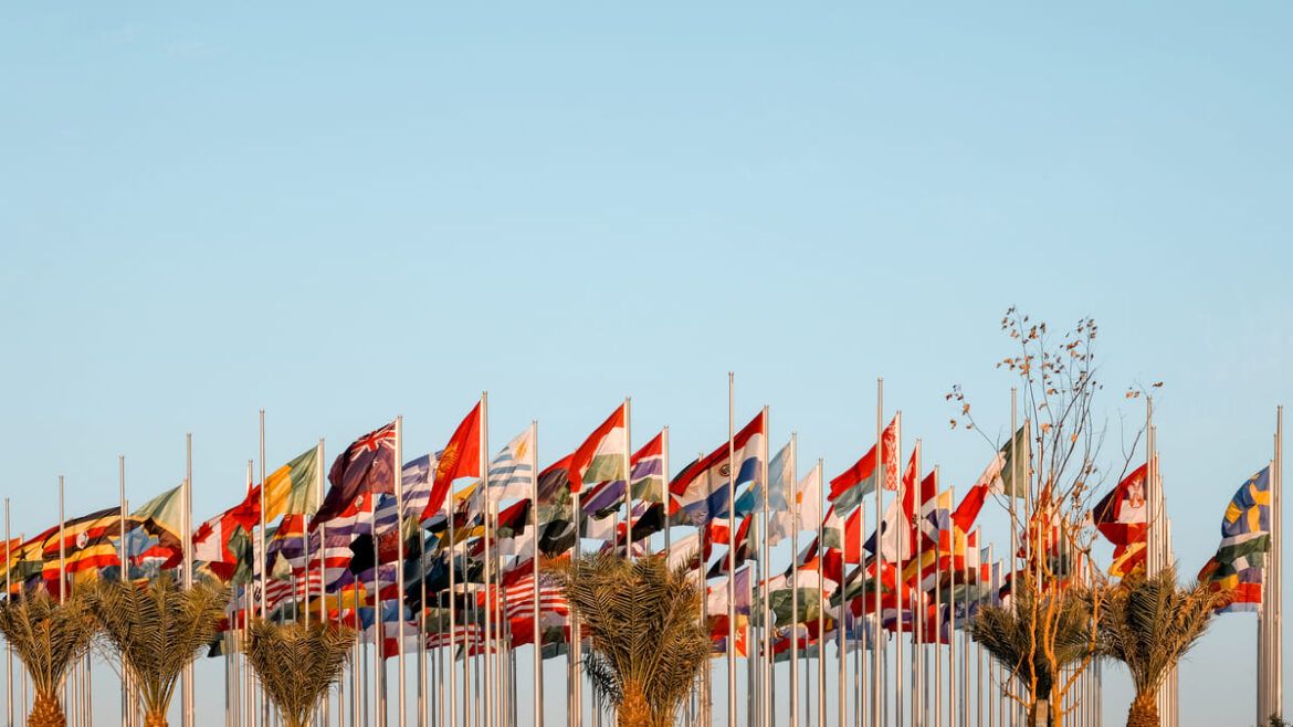 Bandeiras de vários países hasteadas contra um céu claro.