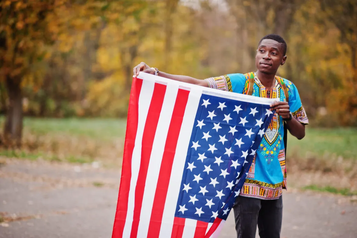 Homem com uma camisa tradicional da África no parque, com bandeira dos EUA.