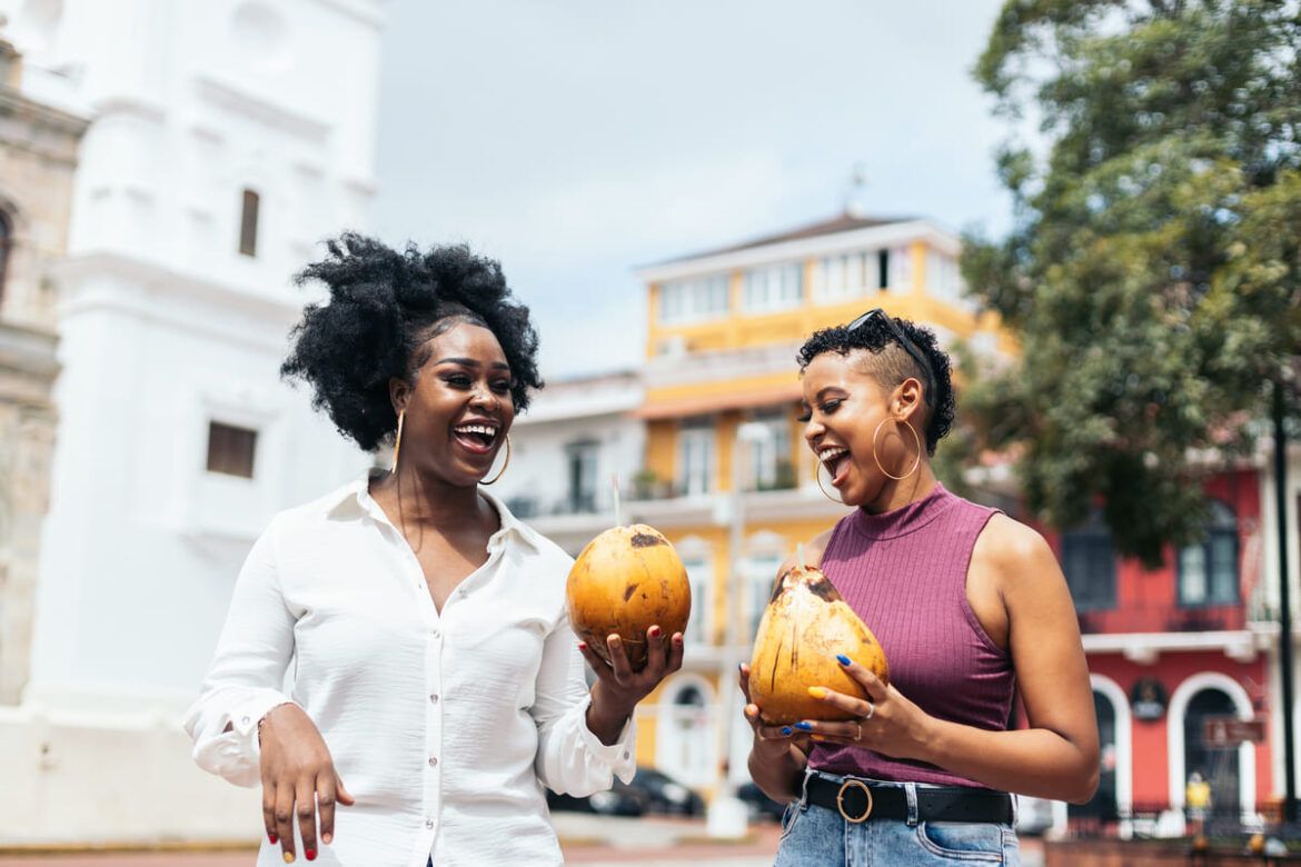 Mulheres latino-americanas elegantes amigas se divertindo andando nas ruas bebendo cocos.