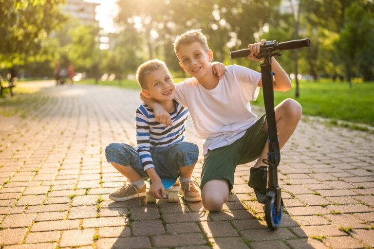 Dois irmãos brincando com patinete e skate em um parque no dia do irmão.