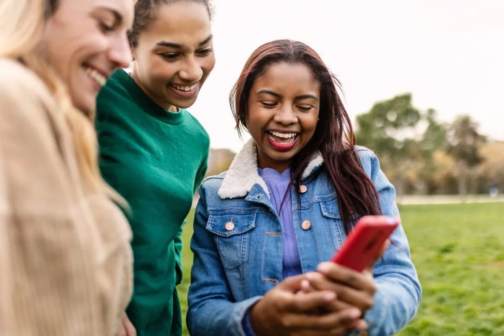 Mulheres sorrindo enquanto visualizam fotos nas redes sociais. 