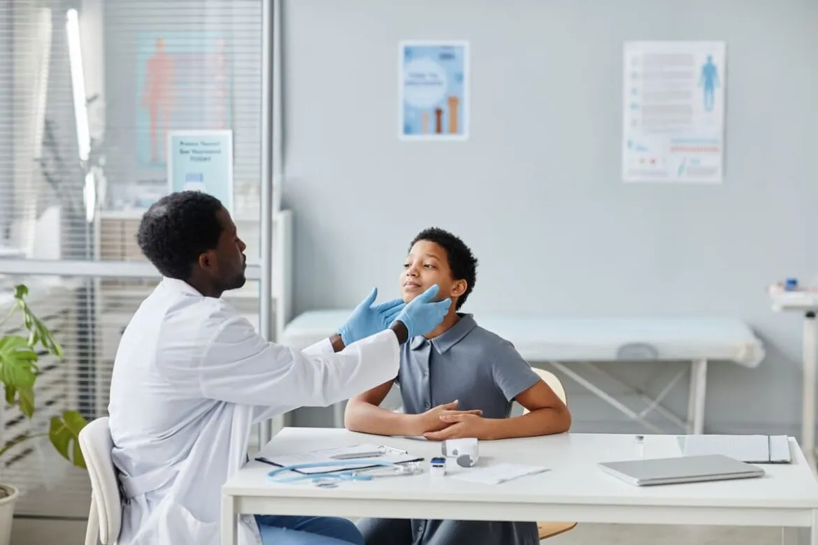 Médico examinando o pescoço de um paciente jovem em consultório.