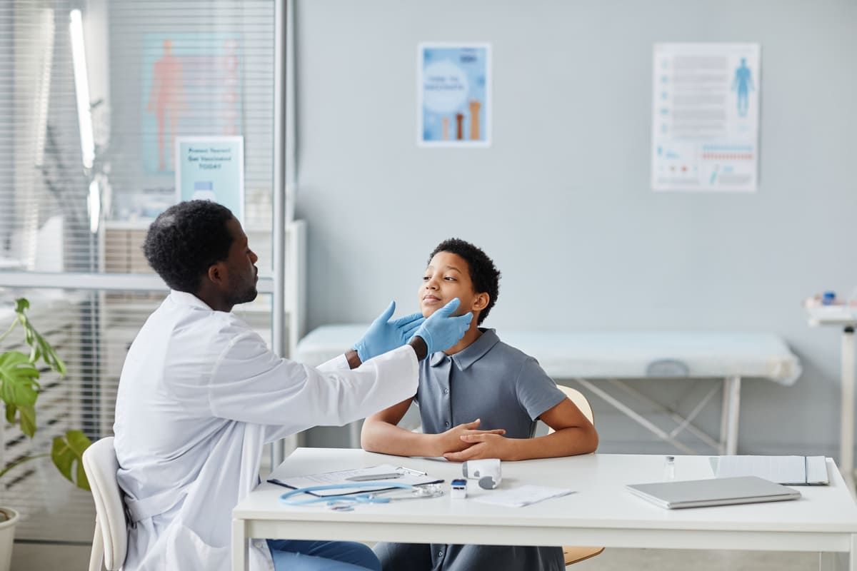 Médico examinando o pescoço de um paciente jovem em consultório.