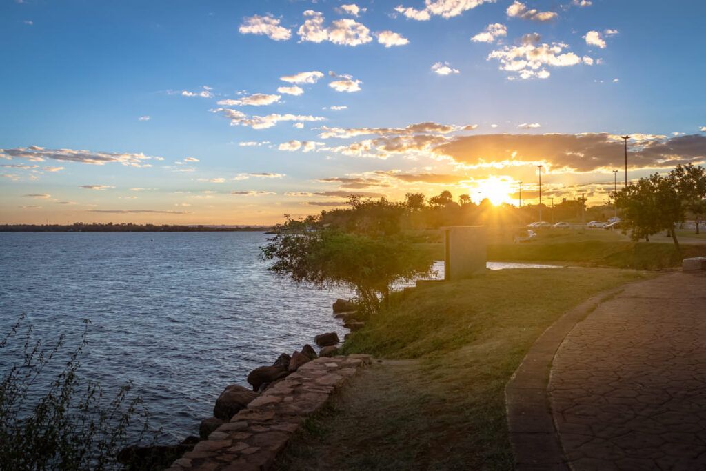 Por do sol em Brasília. O lago está calmo e há árvores no cenário