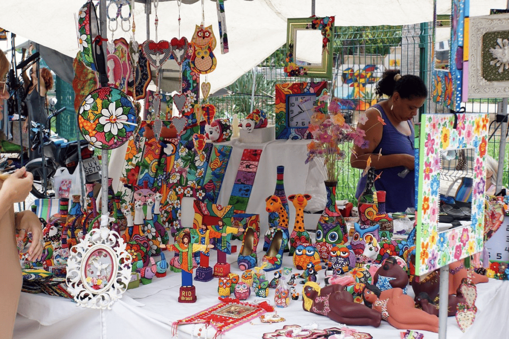 Feira Hippie da Praia de Ipanema, a foto mostra uma tenda com muitos objetos pendurados e dispostos em uma mesa com pano branco