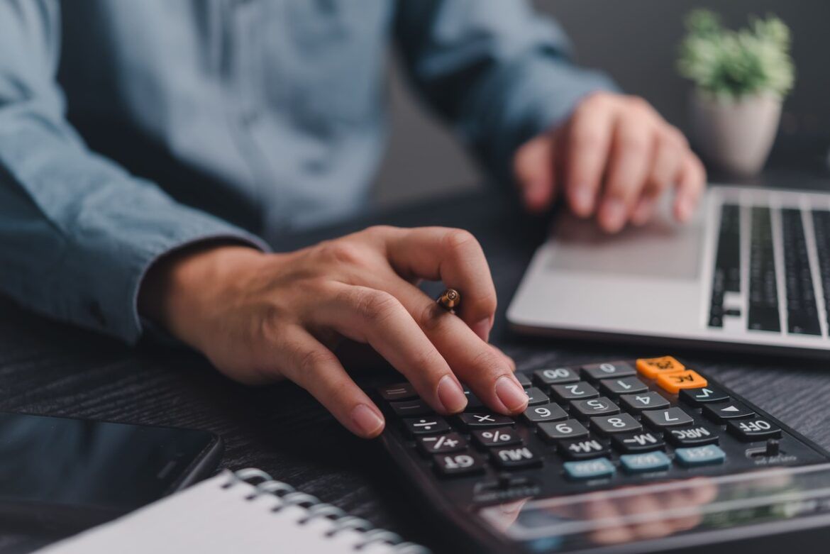 Homem usando calculadora e notebook para calcular a folha de pagamento.