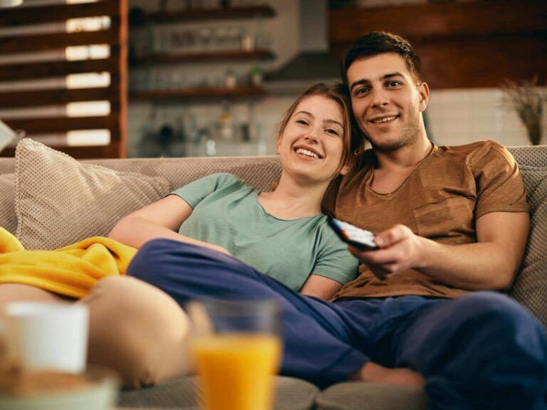 Casal vendo filmes para aprender inglês na televisão enquanto estão deitados confortavelmente no sofá