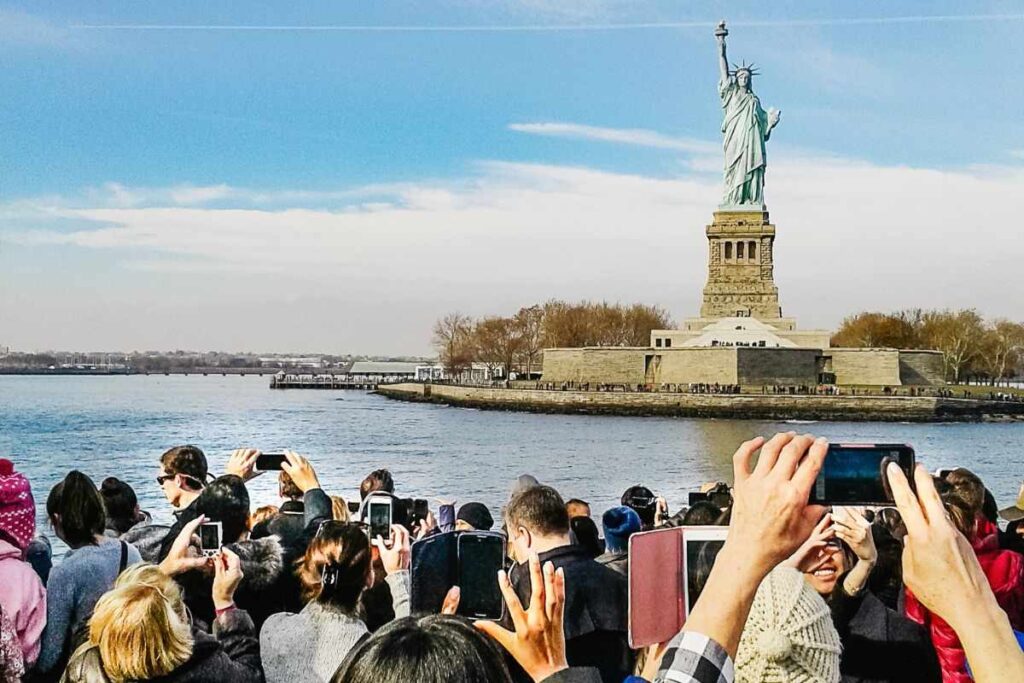 Pessoas tirando foto da Estátua da Liberdade e criando frase para a foto em Nova York.